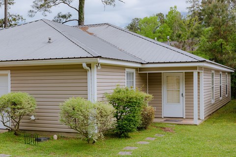 a small tan house with a metal roof on a lawn