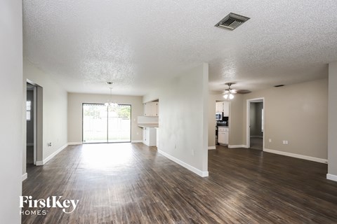 an empty living room with wood flooring and a kitchen