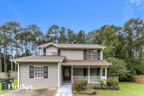 a small gray house with a porch and a lawn and trees