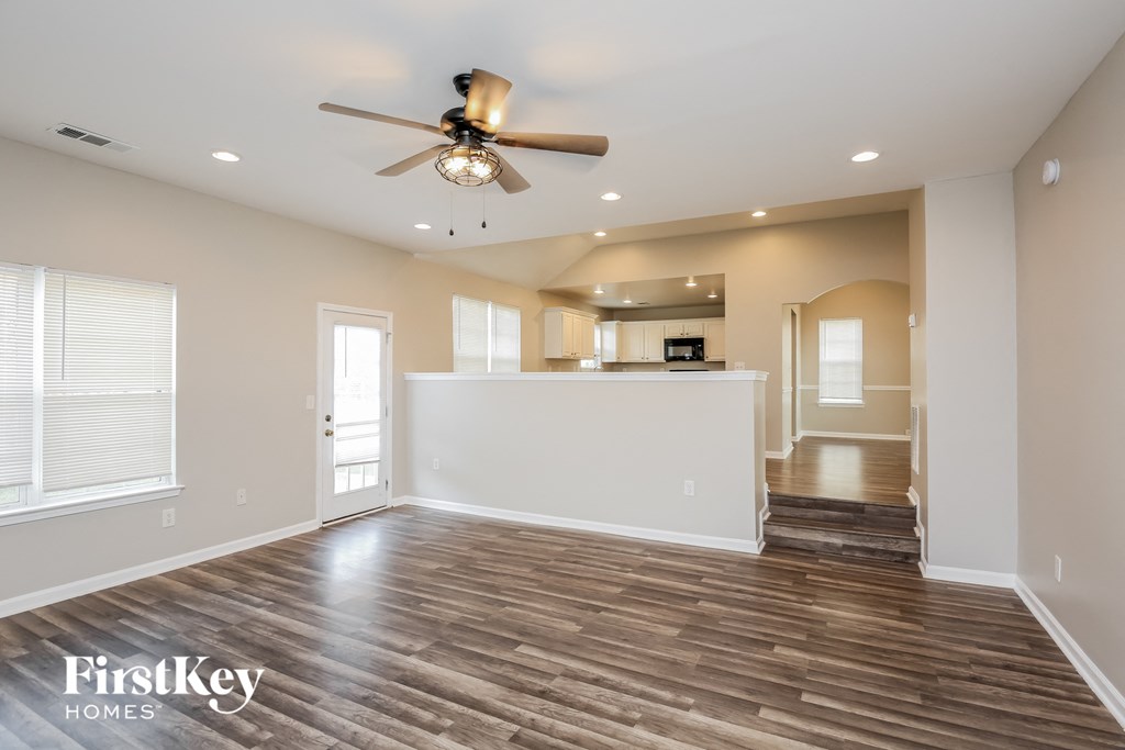 an empty living room with a ceiling fan and a kitchen