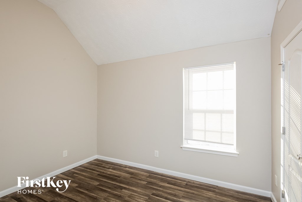 a bedroom with a wood floor and white walls and a window