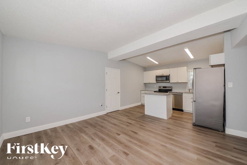 the living room and kitchen of an apartment with wood flooring and stainless steel appliances