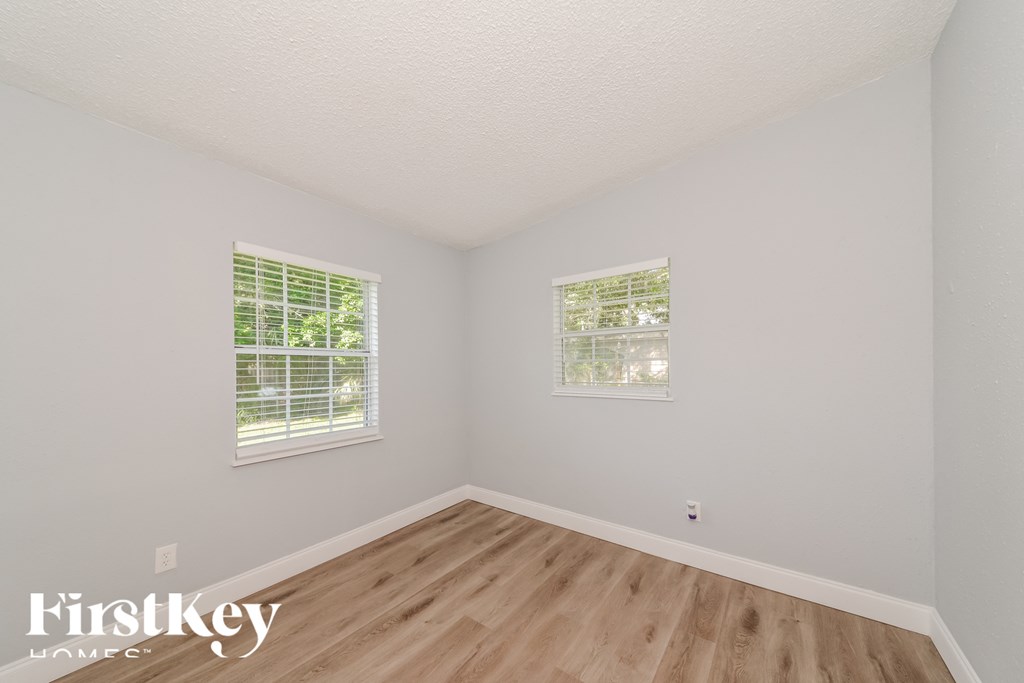 a bedroom with a hard wood floor and two windows