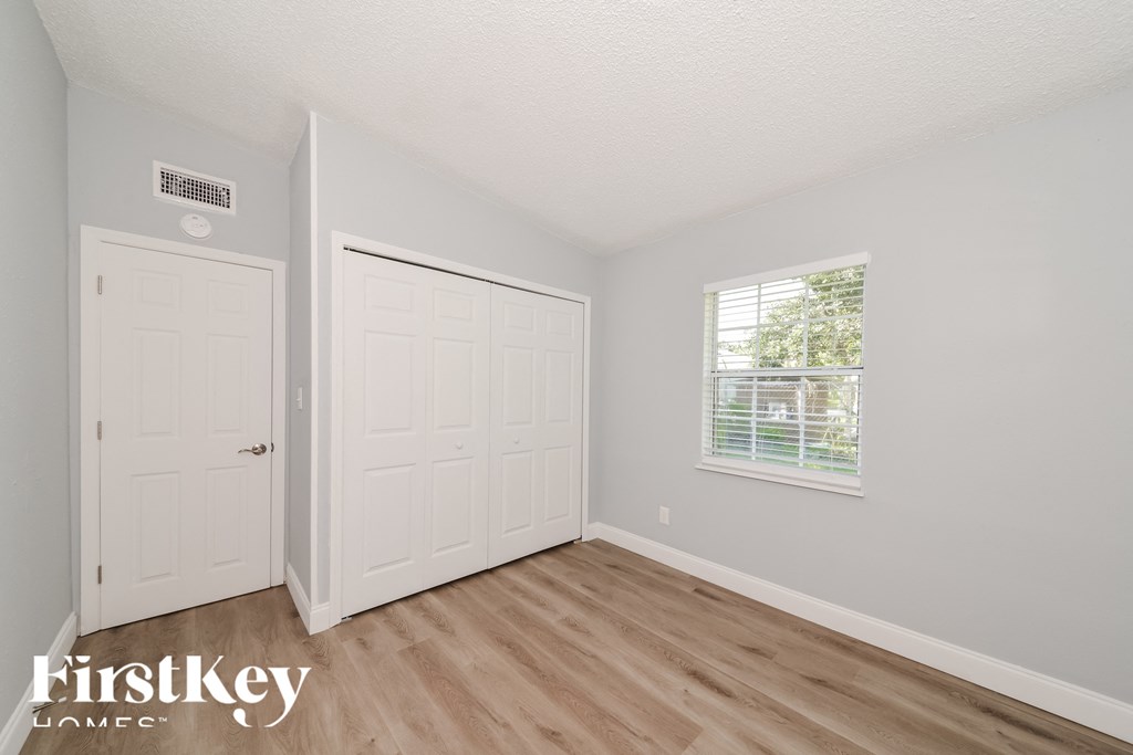 a bedroom with white walls and wood floors and a window