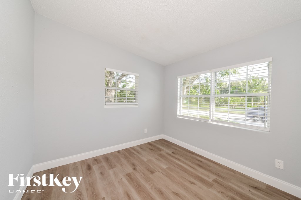 a bedroom with wood floors and white walls and two windows