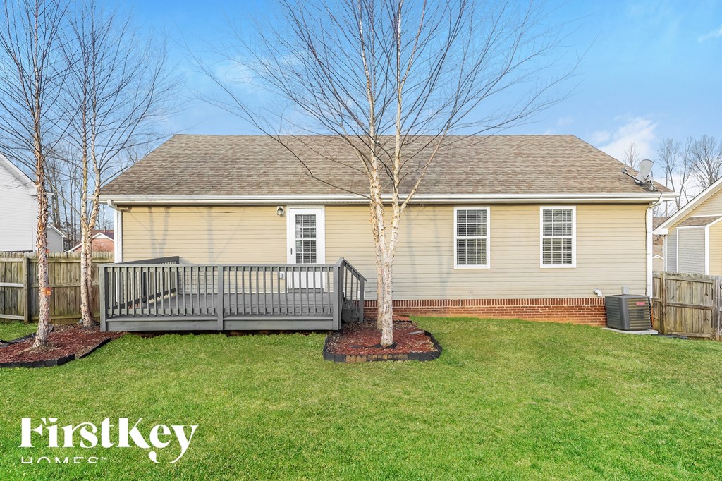the front of a yellow house with a deck and a tree