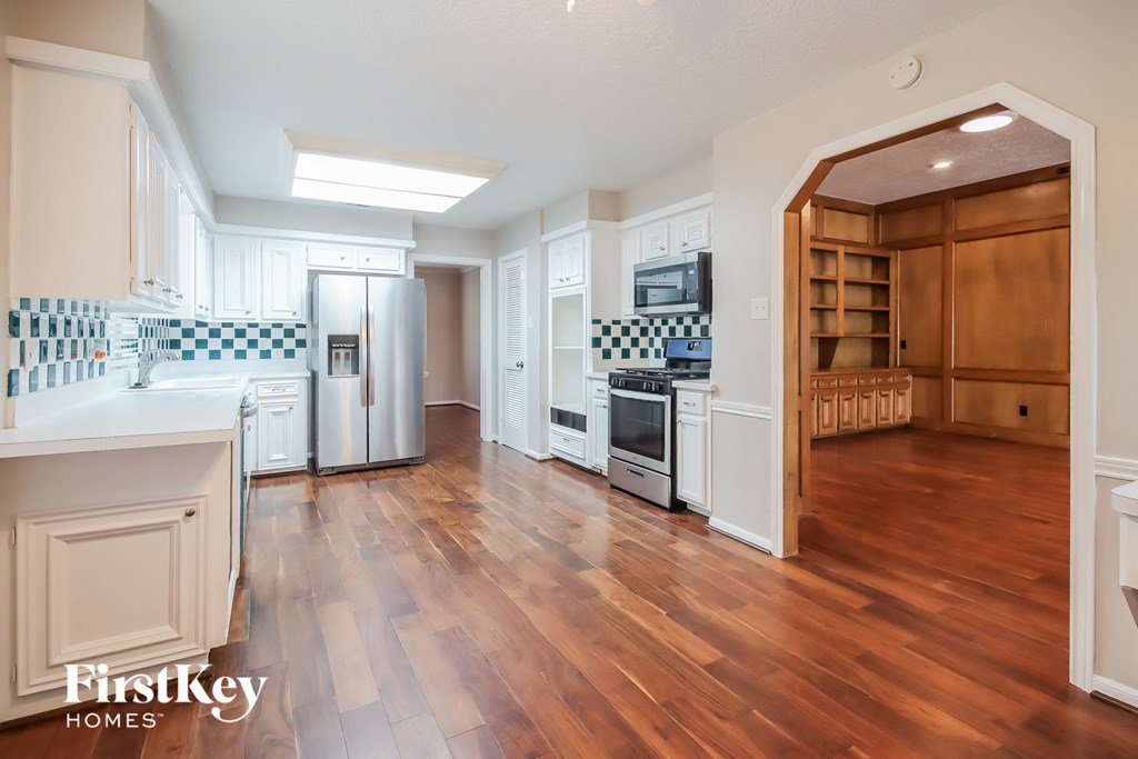 an open kitchen and living room with hardwood flooring and white cabinets