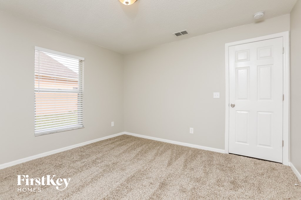 a bedroom with carpet and a white door and a window