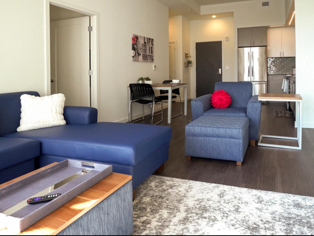 a living room with blue couches and a table and a kitchen