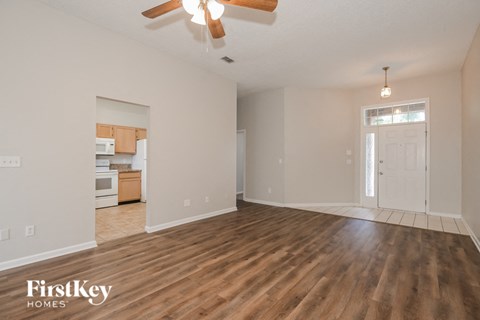 an empty living room and kitchen with wood flooring and a ceiling fan