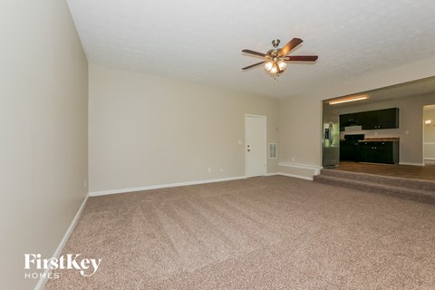 a spacious living room with carpet and a ceiling fan