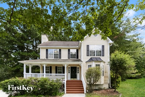 A two-story house with a porch and a tree in front.