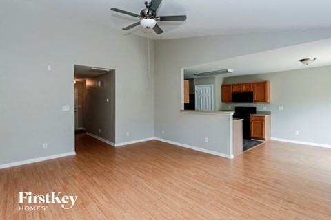 an empty living room and kitchen with wood floors and a ceiling fan