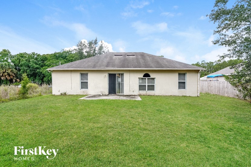 the backyard of a small white house with a grassy yard