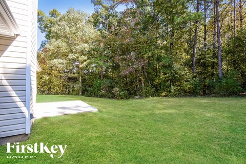 a backyard with green grass and trees and a white house