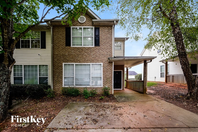 A brick house with a black door and windows is surrounded by trees.