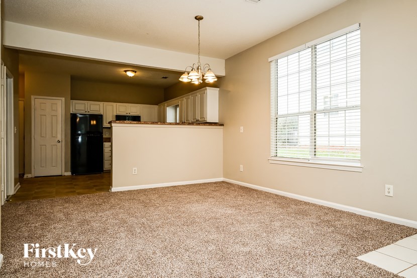 A spacious room with a kitchen area and a window with blinds.