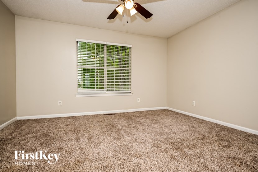 A room with a carpeted floor, a ceiling fan, and a window with blinds.