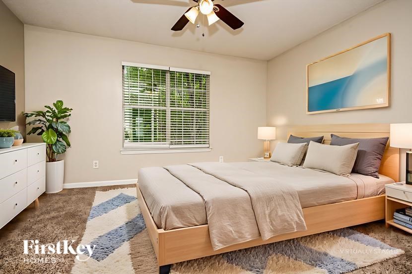 A bedroom with a bed, a ceiling fan, and a painting on the wall.
