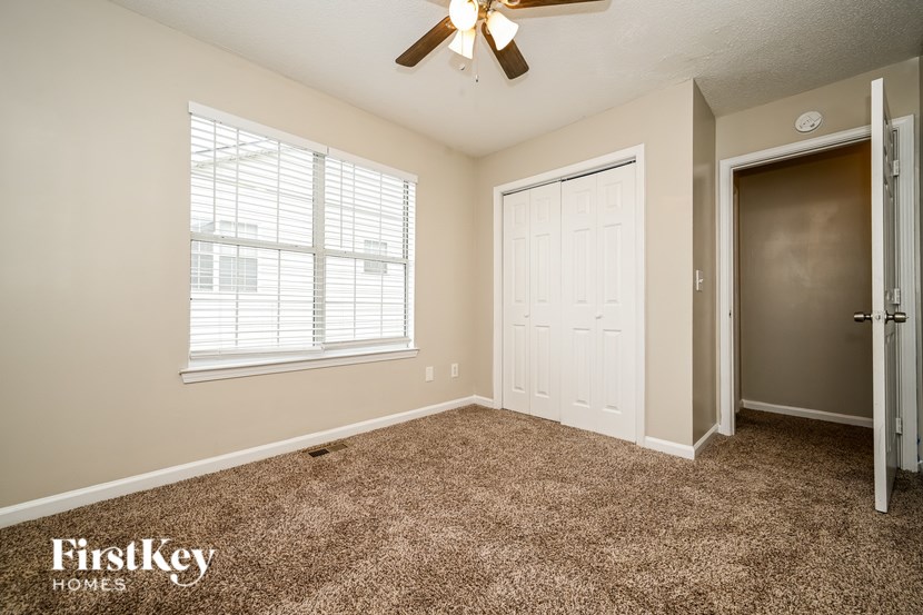 A room with a carpeted floor, a ceiling fan, and a window with blinds.