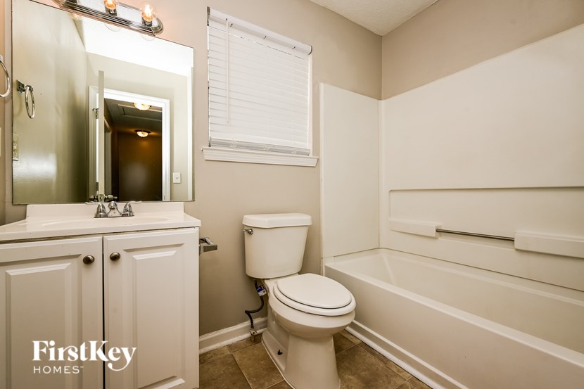 A white toilet sits in a bathroom with a white sink and a white bathtub.