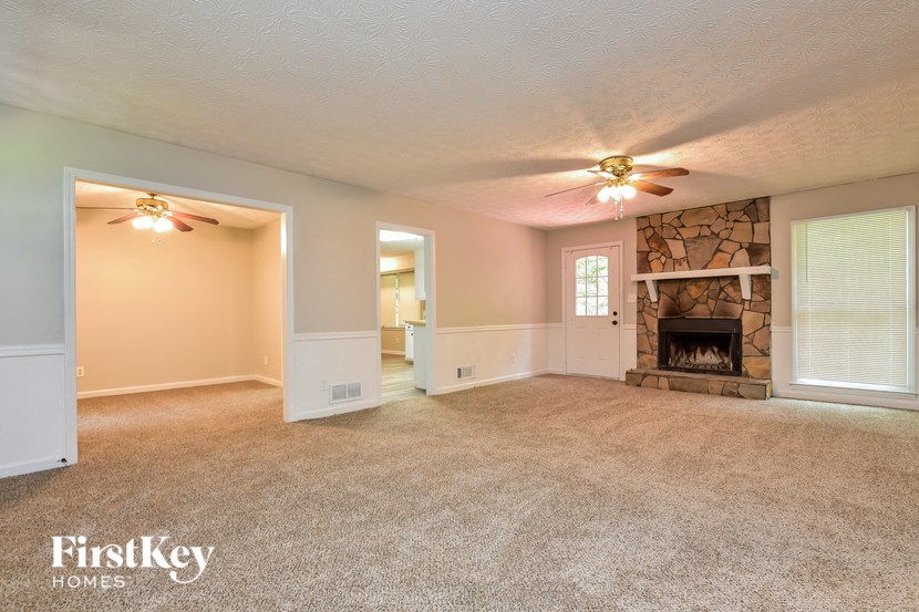 an empty living room with a fireplace and two ceiling fans