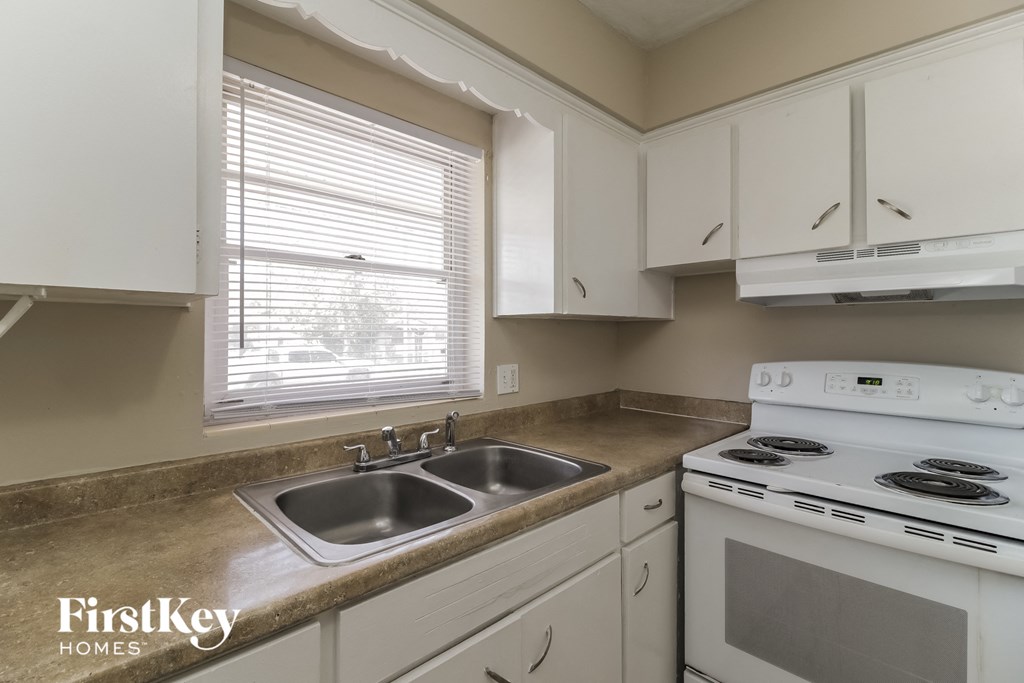 A kitchen with a stove, sink, and cabinets.
