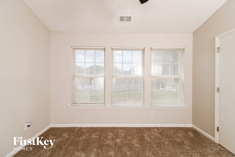 a living room with carpet and three windows