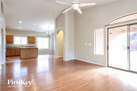 an empty living room with a kitchen and a ceiling fan