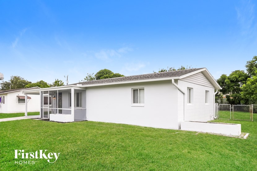 A white house with a porch and a fence in the front yard.
