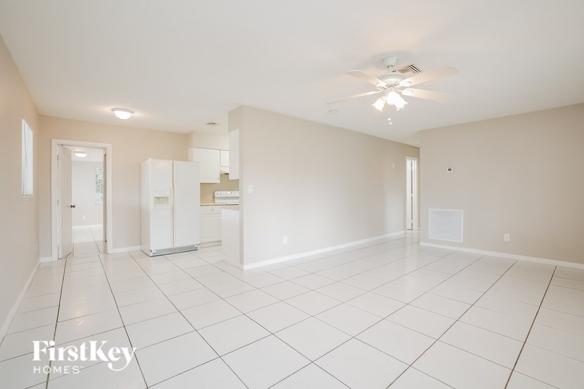 A spacious empty room with a ceiling fan and a refrigerator in the corner.