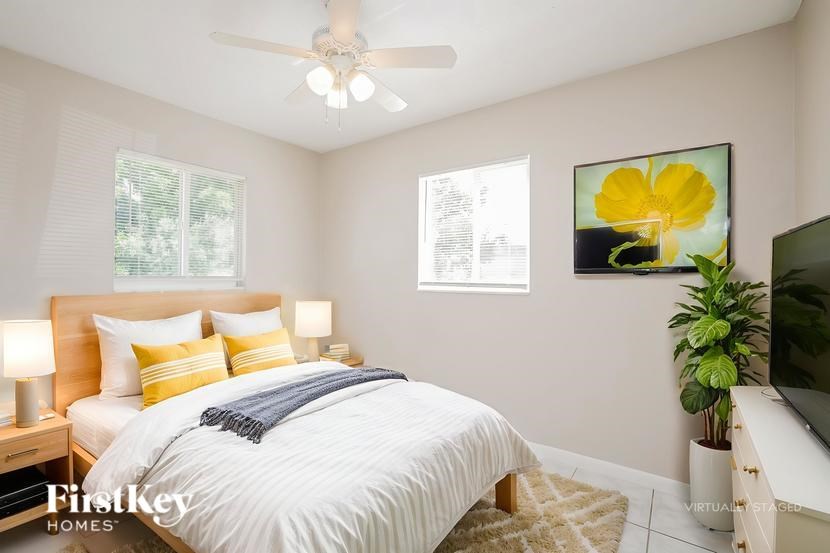 A bedroom with a bed, a ceiling fan, and a painting of a yellow flower.