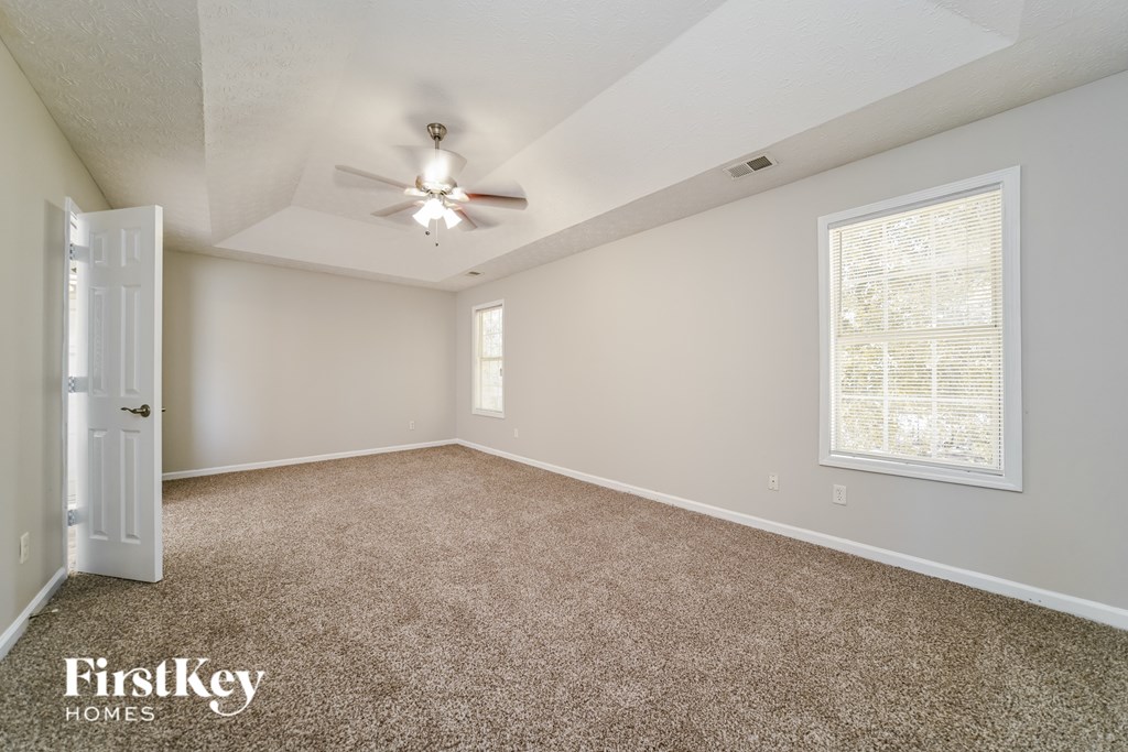 A room with a carpeted floor, a ceiling fan, and a window with blinds.