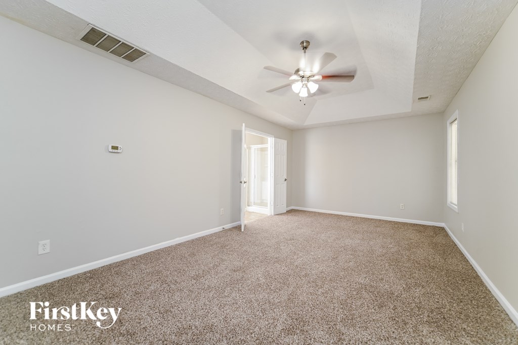 A carpeted room with a ceiling fan and a doorway leading to another room.