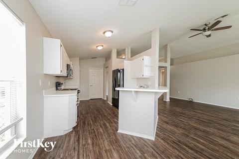 A spacious kitchen and living room with wood flooring and white cabinetry.