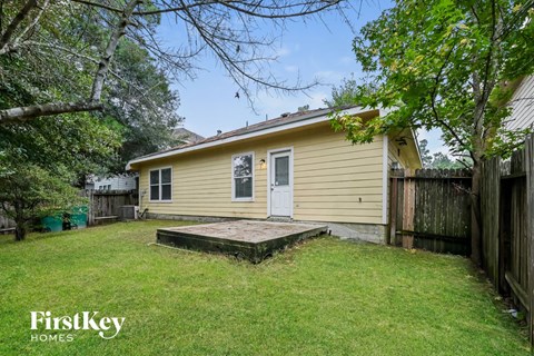 A small house with a porch is surrounded by a fence and trees.