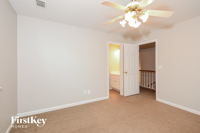 a bedroom with white walls and a ceiling fan and a door to a nursery