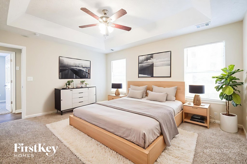 A bedroom with a large bed, a ceiling fan, and a potted plant.
