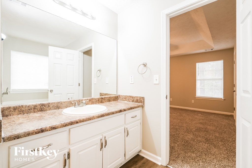 A bathroom with a sink, mirror, and a carpeted floor.