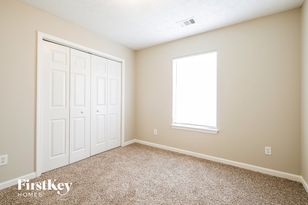 A room with a carpeted floor, a white door, and a window with a white frame.