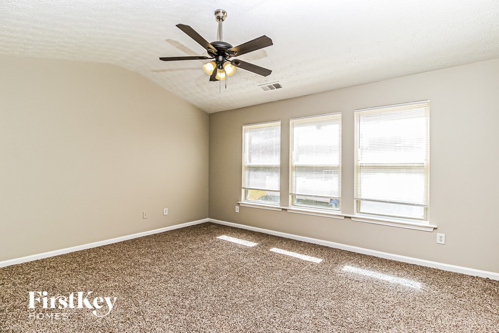 A room with a ceiling fan and three windows.