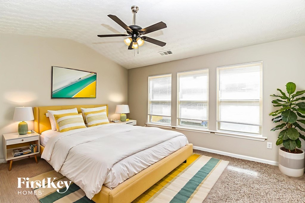 A bedroom with a bed, a ceiling fan, and a painting on the wall.