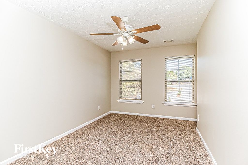 A room with a ceiling fan and two windows.