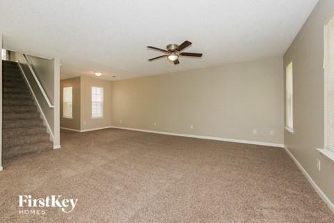 an empty living room with a ceiling fan and a staircase