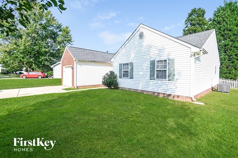 a white house with a yard and a red car in the background