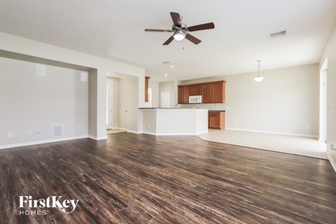 an empty living room with a ceiling fan and a kitchen