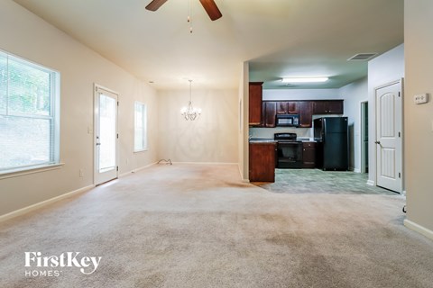A spacious living room with a ceiling fan and a kitchen in the background.