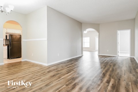 A spacious room with wooden flooring and a refrigerator in the corner.