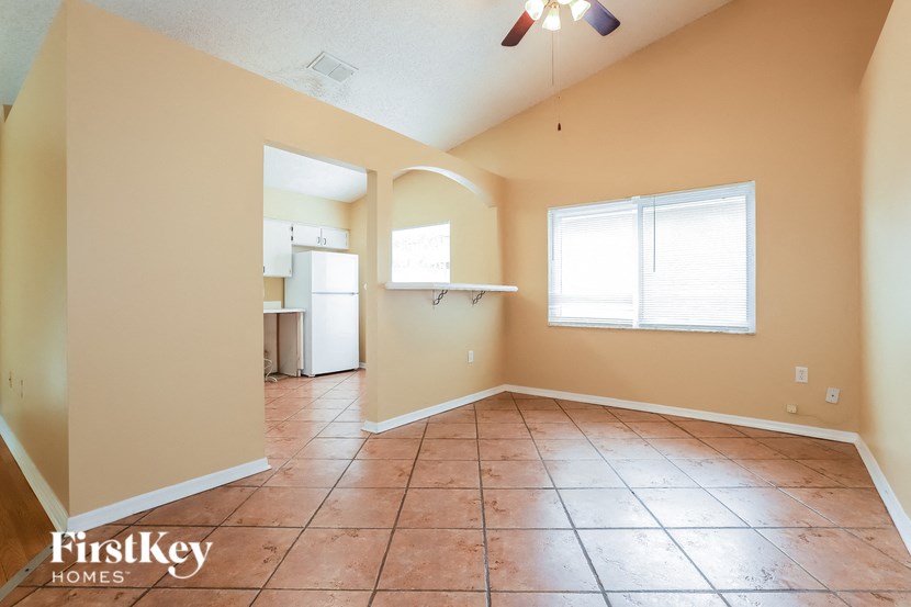 an empty living room with a kitchen and a ceiling fan