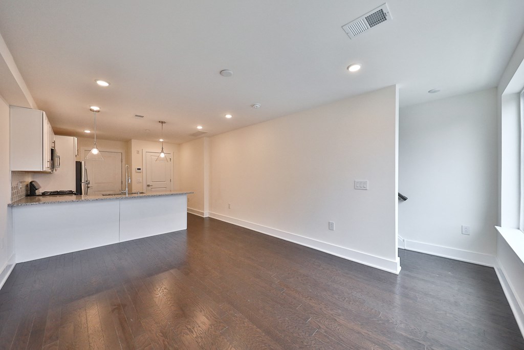 the living room and kitchen of an empty home with white walls and wood flooring